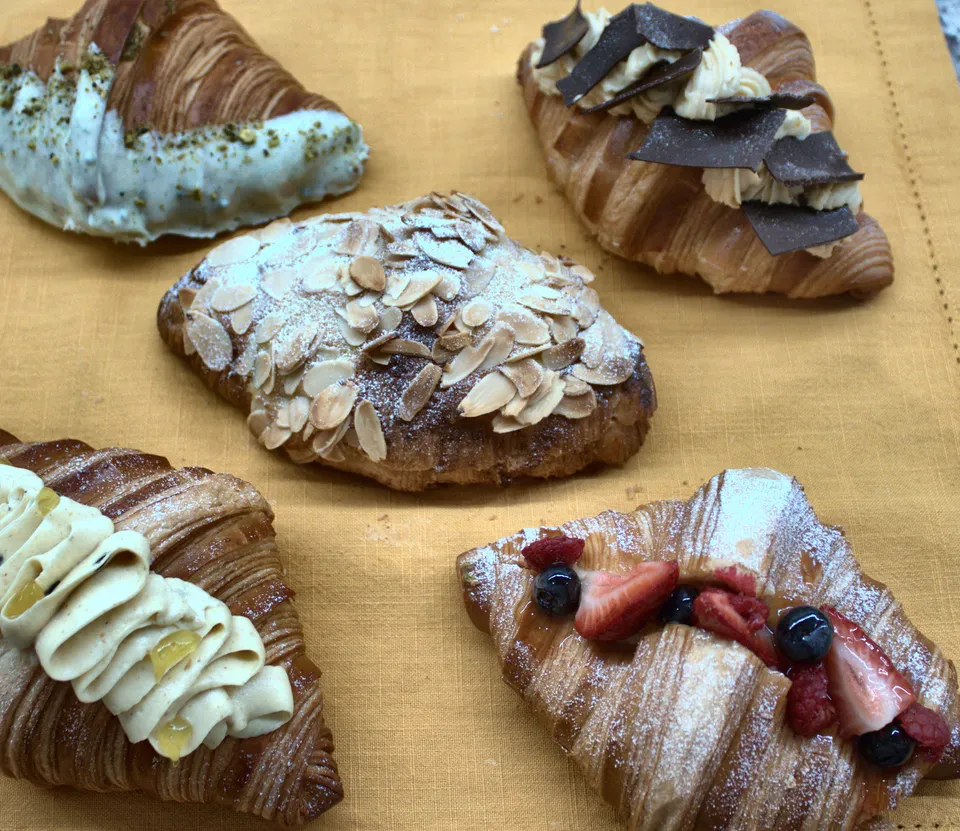Seis croissants de especialidad sobre un mantel dorado, vistos desde arriba