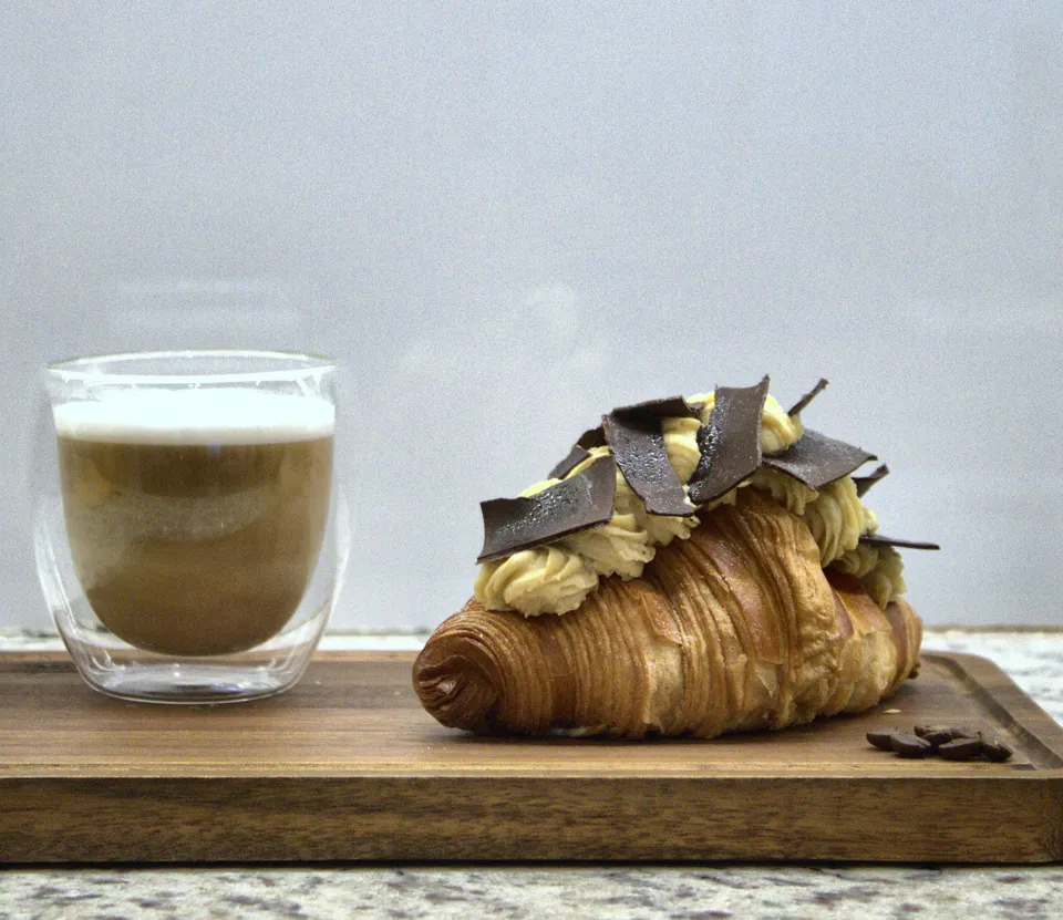 Croissant con crema y láminas de chocolate junto a un café con leche