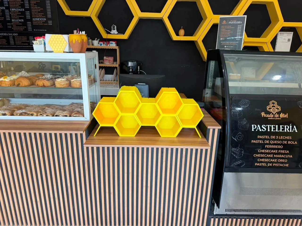 El mostrador de Pecado de Miel: barra de madera a rayas, panal amarillo sobre la barra y repisas de hexágonos en la pared negra
