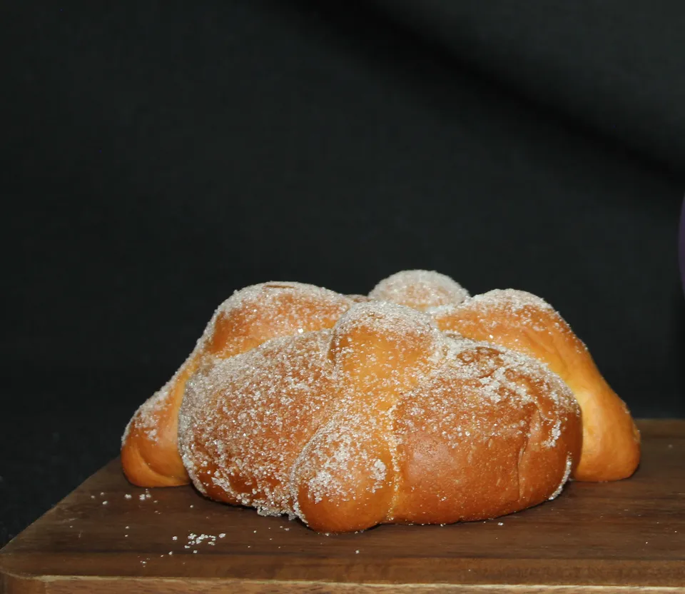 Pan de muerto entero con sus huesitos, cubierto de azúcar, sobre una tabla de madera